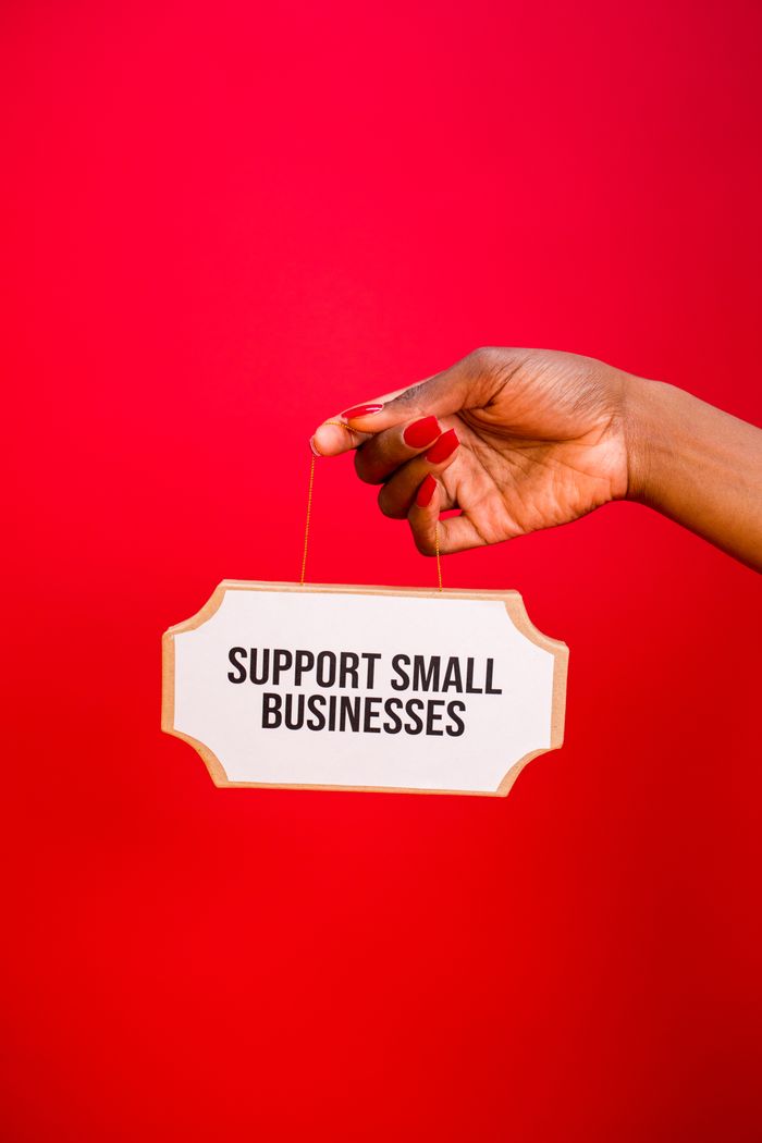 A hand holding a sign that encourages support for small businesses, set against a bold red background.
